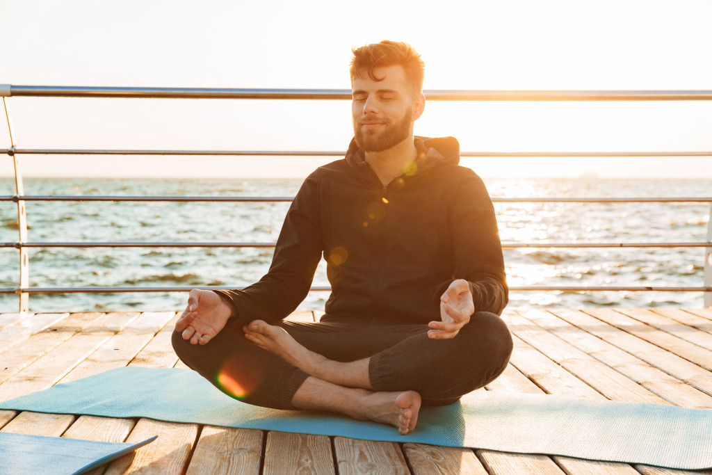 man meditating in a yoga mat at sunrise near body of water